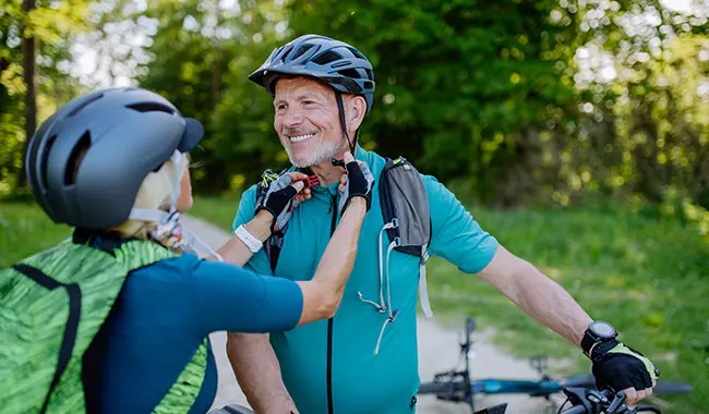 senior man with bike and woman helping put on his bike helmet