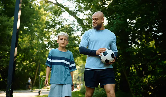 middle age man holding soccer ball walking with son